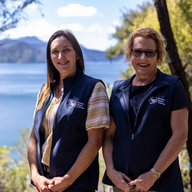 Two women standing infront of sea and mountains